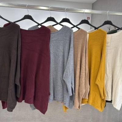 Casacos de malha em várias cores pendurados em cabides numa barra metálica