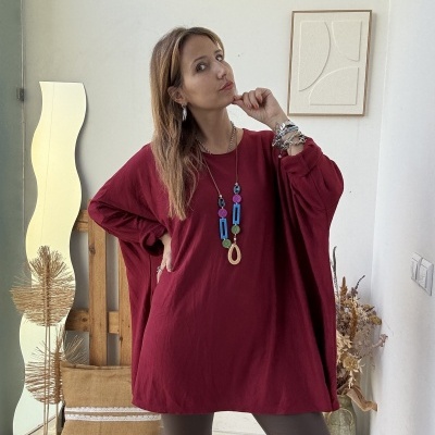 Mulher com túnica vermelha e colar colorido em ambiente interior neutro