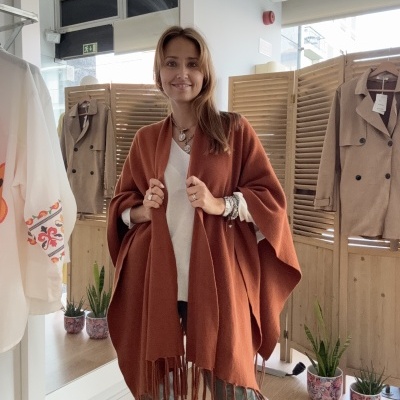 Manta castanha com franjas numa mulher numa loja com casacos e plantas no fundo