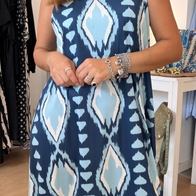 Vestido azul com padrão geométrico usado por mulher com joias, em loja de roupa.
