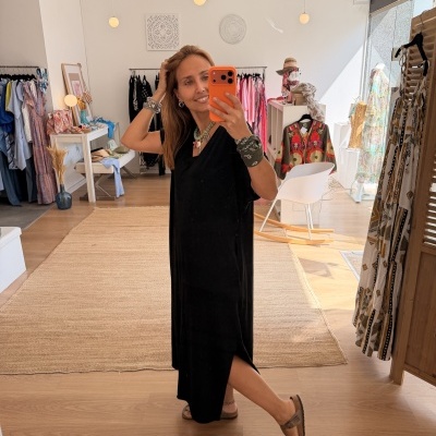 Mulher com vestido preto tirando selfie em loja de roupa com decoração clara e roupas coloridas em cabides