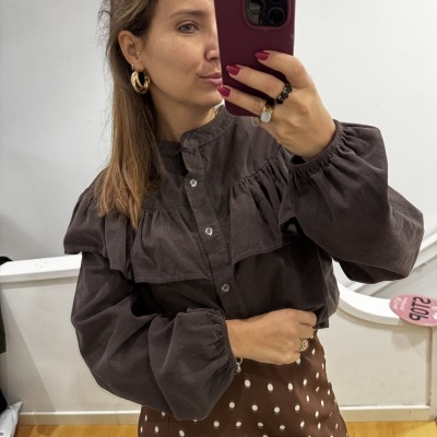 Mulher a tirar selfie vestindo blusa castanha de veludo com botões e saia castanha às bolinhas brancas