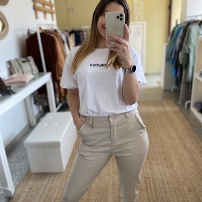 Pessoa a usar t-shirt branca com texto e calças beges num espaço interior com roupas ao fundo