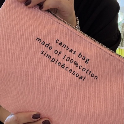 Bolsa em lona rosa com texto em preto, segurada por mãos femininas com unhas castanho escuro.