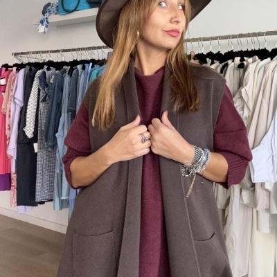 Mulher com colete castanho e chapéu largo castanho numa loja de roupa.