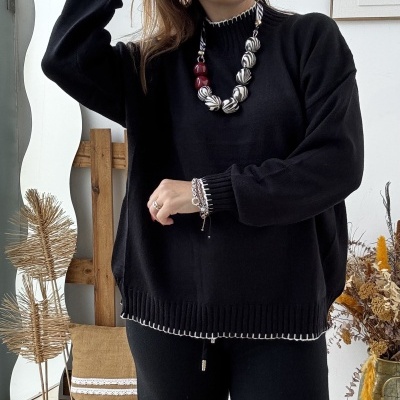 Mulher com conjunto preto detalhe branco e colar bolas coloridas em ambiente rústico