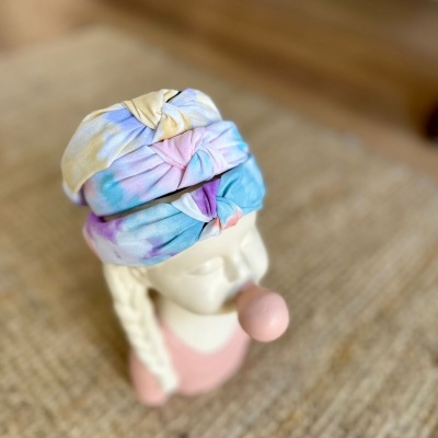 Três faixas tie-dye em tons pastel sobre cabeça de escultura branca com bola cor de rosa na boca