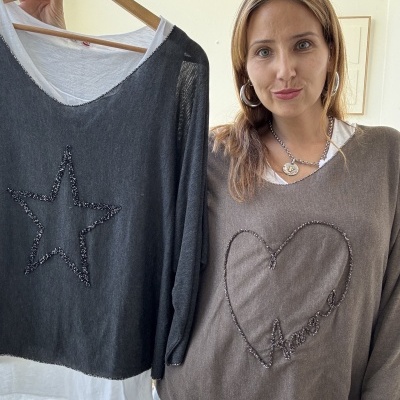 Mulher com blusa castanha segurando blusa preta com estrela em cabide