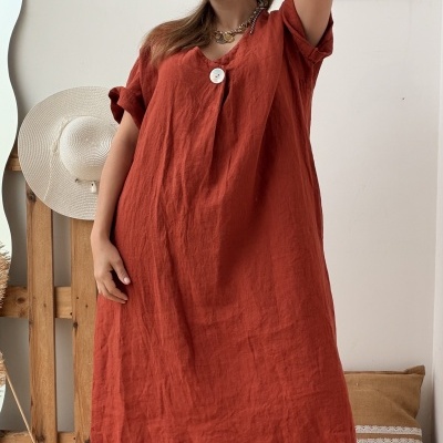 Vestido vermelho de linho com botão grande branco ao centro em ambiente interior