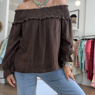 Blusa castanha ombro a ombro com folhos e jeans azuis claros usada por mulher