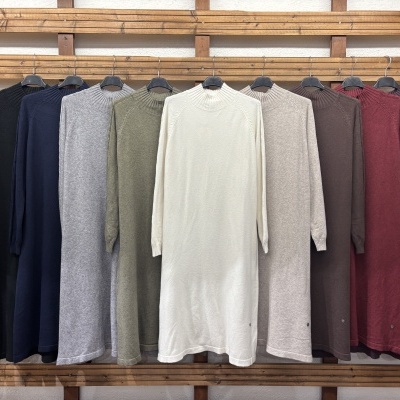 Vestidos de malha de várias cores pendurados em cabides numa prateleira de madeira