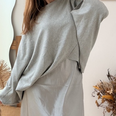 Mulher com vestido cinzento claro e camisola cinzenta de malha, óculos de tartaruga e pulseiras.