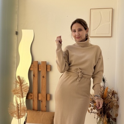 Mulher a usar vestido comprido bege de malha com gola alta e cinto