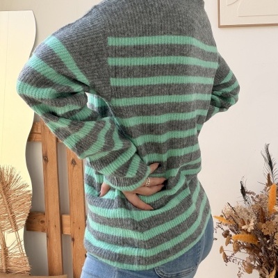 Mulher com camisola de malha cinza e verde-água e jeans azuis claros em ambiente interior minimalista