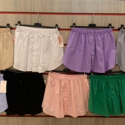 Nove calções de várias cores pendurados em cabides numa parede de ripas vermelhas.