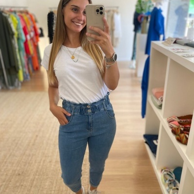 Mulher com blusa branca e jeans azul de cintura alta numa loja de roupas.