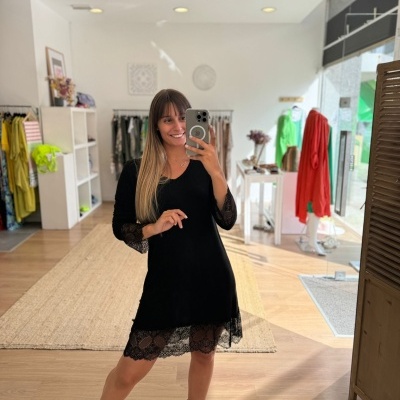 Mulher a usar vestido preto com detalhes em renda a tirar foto em espelho numa loja de roupa.