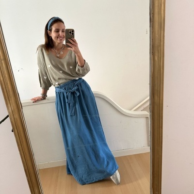 Mulher com camisola bege e saia azul a tirar selfie num espelho com moldura dourada