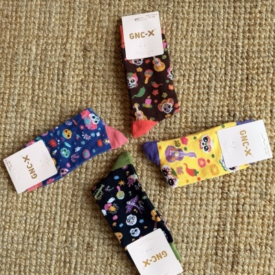 Quatro pares de meias coloridas com padrões de caveiras e instrumentos musicais sobre tapete bege