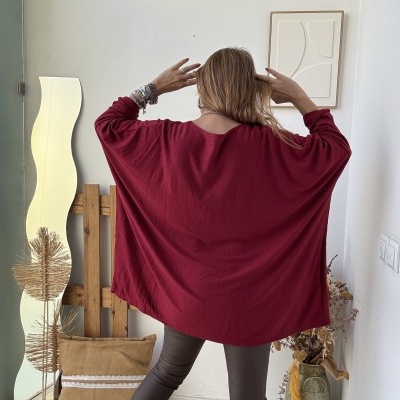 Pessoa vista de costas com camisola vermelha larga e calças castanho-escuro em interior decorado