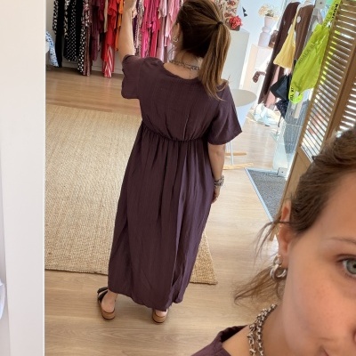 Mulher de costas a tirar selfie num vestido roxo escuro comprido de manga curta e sandálias pretas numa loja de roupa.