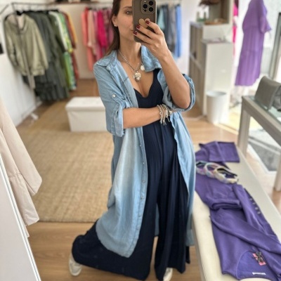 Mulher com vestido azul escuro e casaco azul claro faz selfie num espelho numa loja de roupa