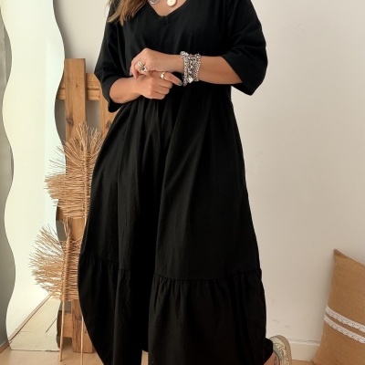Mulher com vestido midi preto, colares coloridos, pulseiras, anéis e ténis brancos com glitter dourado em interior com espelho ondulado.