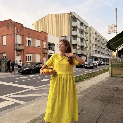 Mulher com vestido amarelo e sapatos pretos segurando cesta de limões na rua