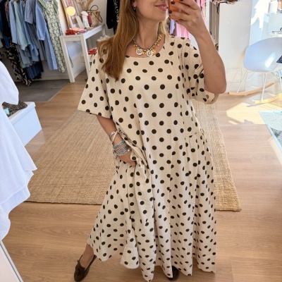 Vestido comprido bege com bolas pretas e mangas curtas, em mulher numa loja de roupa.