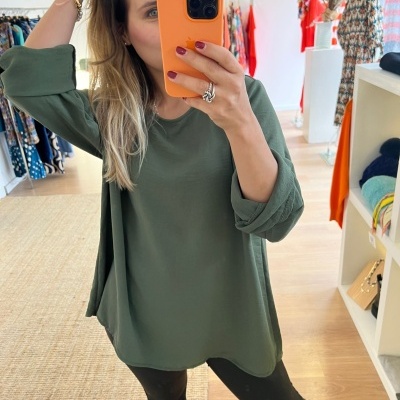 Mulher a vestir túnica verde, leggings pretas e botas castanhas em loja de roupas