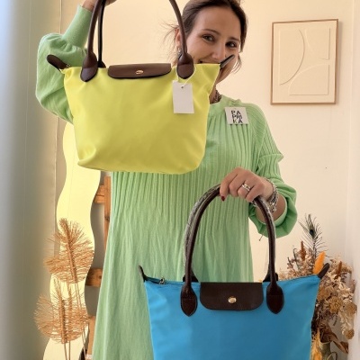 Mulher segura duas malas de mão em nylon, uma amarela e uma azul, com alças castanhas.