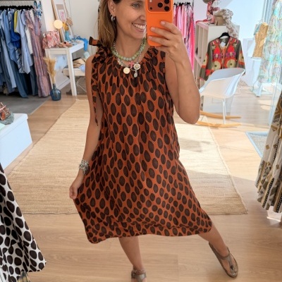 Vestido alaranjado com bolinhas pretas usado por mulher num espelho numa loja