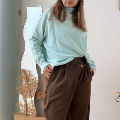 mulher com camisola azul clara e calças castanho em interior