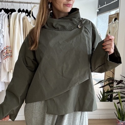 Mulher a usar casaco verde-oliva e saia cinza em loja com roupas e plantas ao fundo