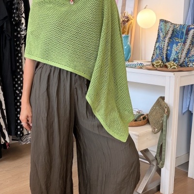Mulher com poncho verde em malha aberta e calças largas castanhas em interior decorado