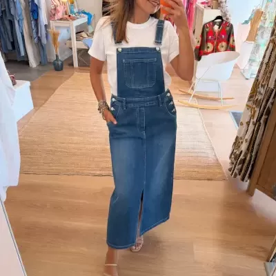 Mulher a tirar selfie usando jardineira azul de ganga e t-shirt branca numa loja de roupa.