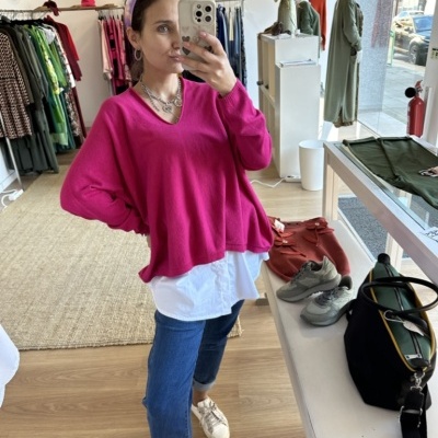 Mulher a tirar selfie em loja com camisola rosa fúcsia, camisa branca e calças de ganga