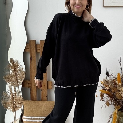 Mulher com conjunto de camisola preta de malha e calças largas pretas, botas castanhas em sala com decoração simples.