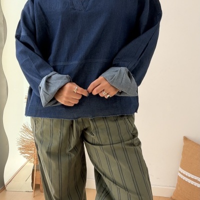 Mulher usando blusa azul escura de tecido grosso e calças verdes com riscas verticais pretas