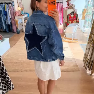 Casaco de ganga azul com estrela escura nas costas usado por mulher num espaço interno de roupa.