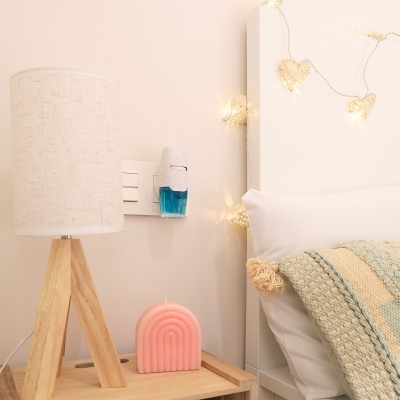 Abajur, vela rosa, recarregador de ar perfumado, almofada branca e manta tecida na cama com luzes em forma de coração