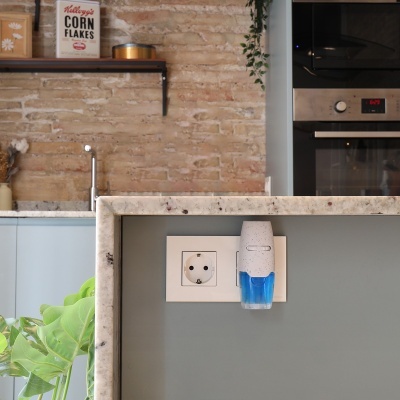 Dispositivo dispensador de aroma branco e azul na tomada da parede cinza clara em cozinha moderna.