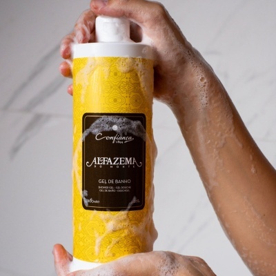 Mãos ensaboadas segurando embalagem amarela de gel de banho com rótulo preto