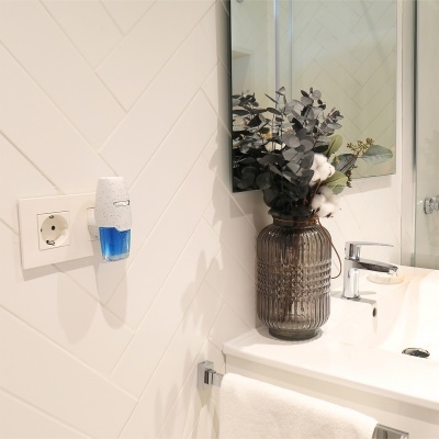Dispositivo de fragrância na tomada junto a lavatório com jarro decorativo e planta artificial