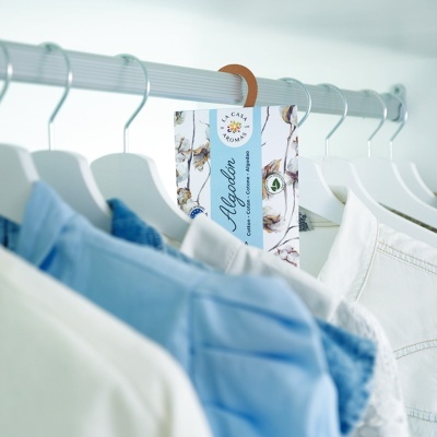 Etiqueta de algodão pendurada na roupa em cabides numa arara branca.