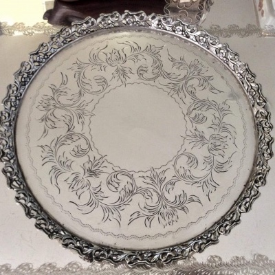 Tabuleiro redondo metálico com borda trabalhada e decoração floral gravada