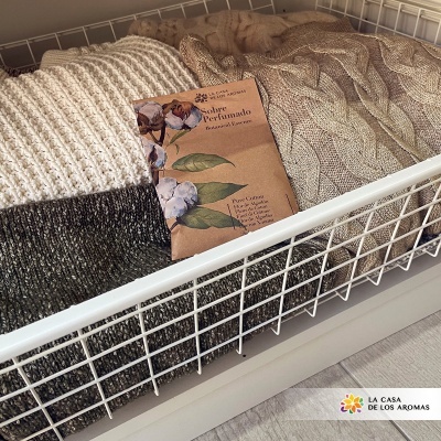 Três mantas de cores neutras em estrutura metálica com etiqueta perfumada