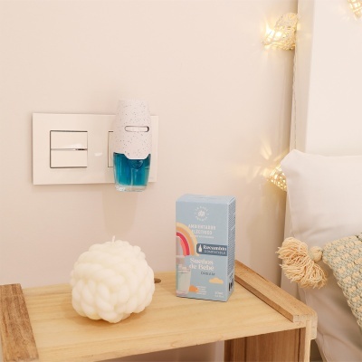 Ambientador elétrico com recarga azul e caixa sobre mesa de madeira ao lado de vela branca e almofada