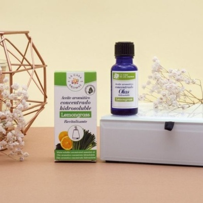 Óleo aromático Lemongrass em frasco azul ao lado da caixa e flores brancas em fundo neutro