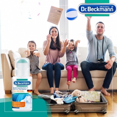 Família em sofá com mala aberta cheia de roupa e produto Dr. Beckmann Quitamanchas Roll-on em primeiro plano